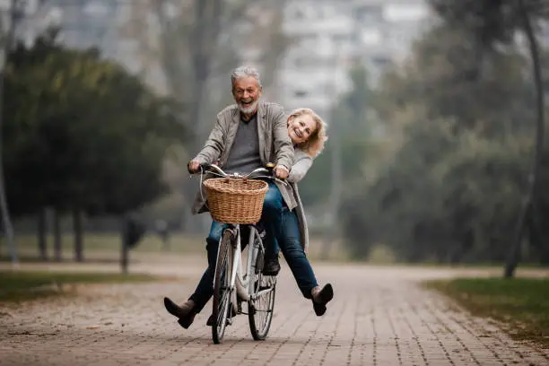 Happy mature couple having fun on a bicycle in autumn day at the park. Copy space.